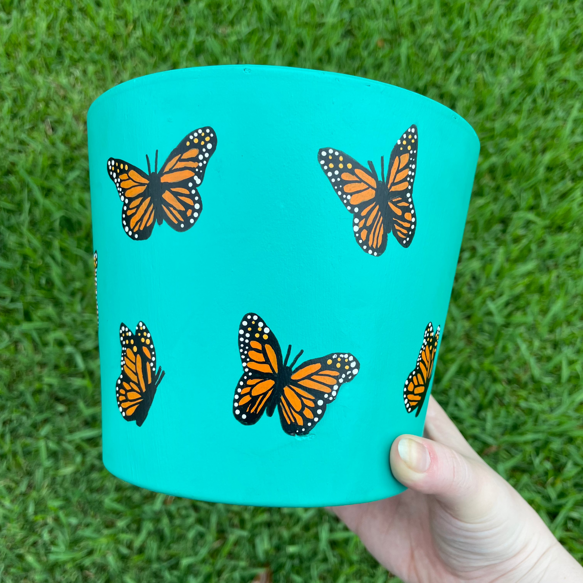 Hand-painted turquoise terracotta pot featuring delicate butterflies and floral accents, creating a whimsical garden-inspired design