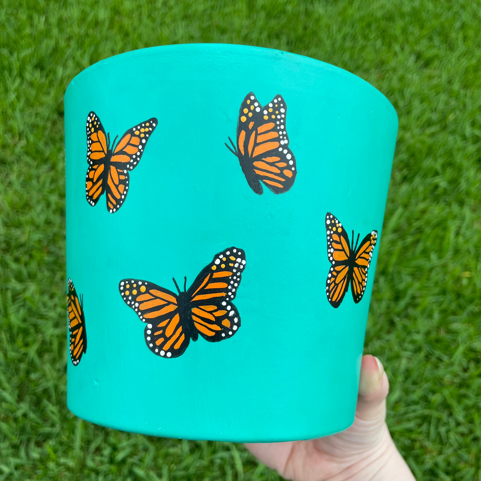 Hand-painted turquoise terracotta pot featuring delicate butterflies and floral accents, creating a whimsical garden-inspired design