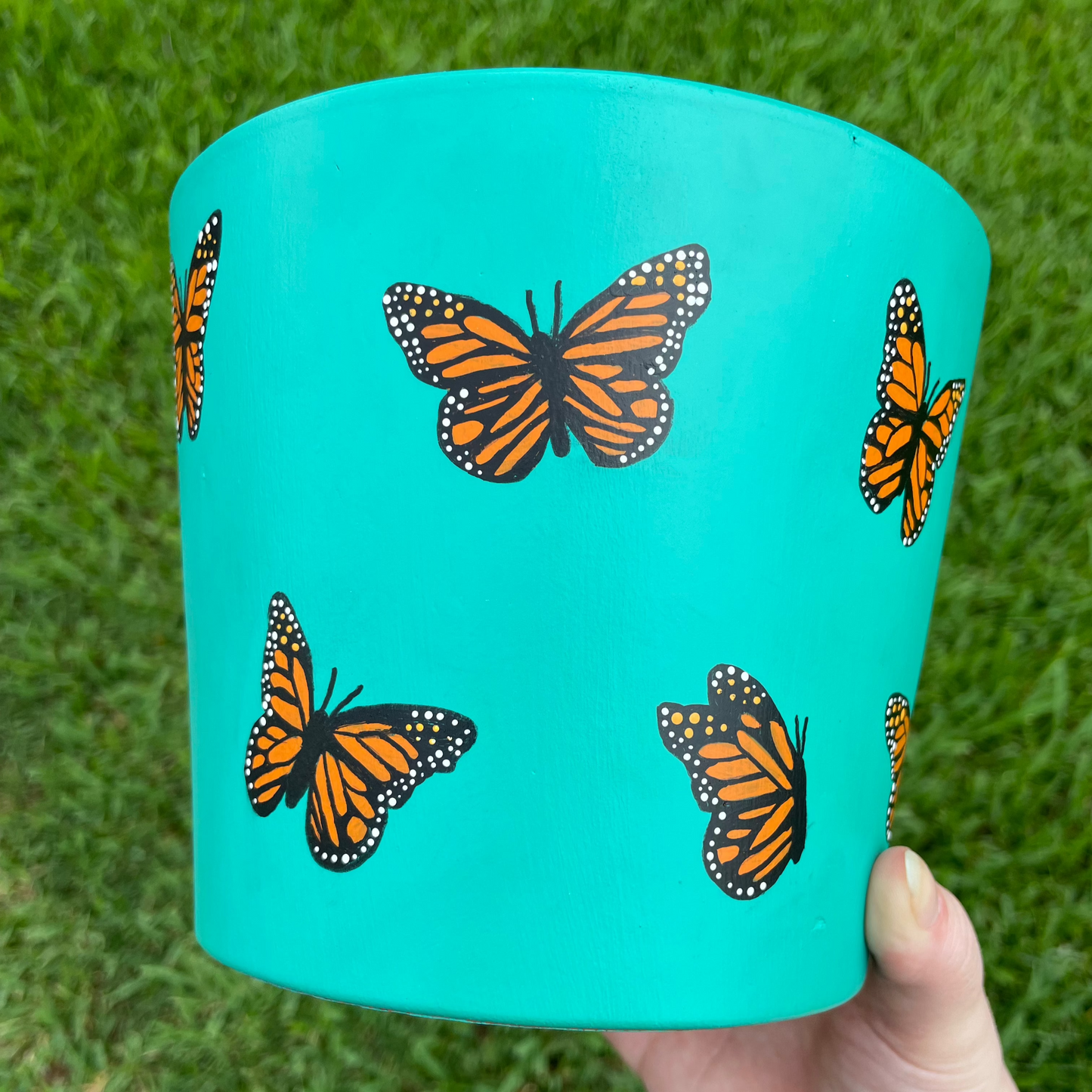 Hand-painted turquoise terracotta pot featuring delicate butterflies and floral accents, creating a whimsical garden-inspired design